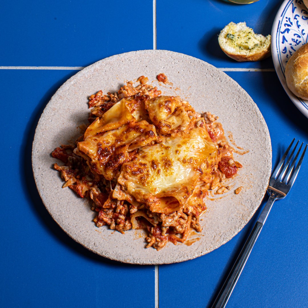 slice of lasagne on a grey plate with a blue backdrop